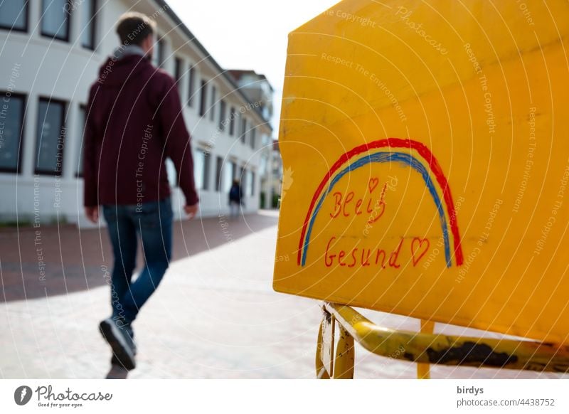 Stay healthy ! Inscription with rainbow on a yellow box. In the background a young man walks by. Corona, Pandemic, Vaccinate corona covid19 inoculate sb.