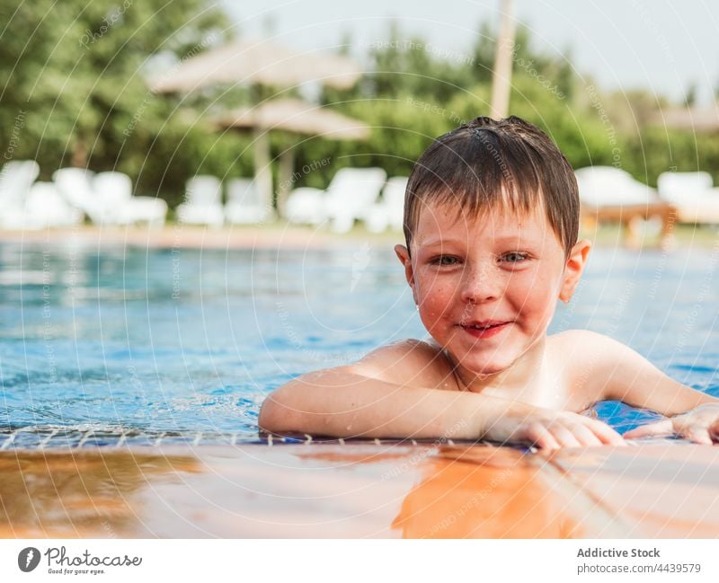 Cheerful boy in swimming pool in summer child poolside cheerful having fun water wet hair kid joy smile weekend happy enjoy pleasure vacation optimist charming