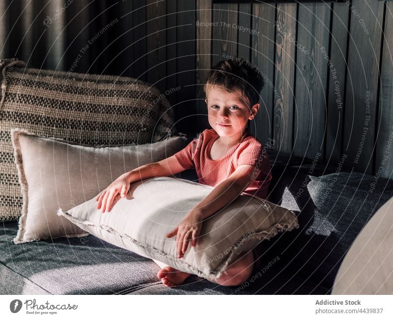 Smiling boy sitting on sofa at home child living room cushion smile cheerful adorable couch kid little childhood comfort pillow soft domestic glad charming cute