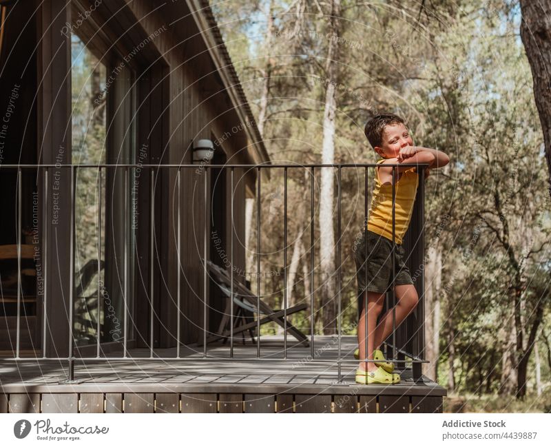 Child standing on terrace of house in forest boy veranda child recreation summer kid peaceful tranquil nature wooden woods woodland summertime sunny sunlight