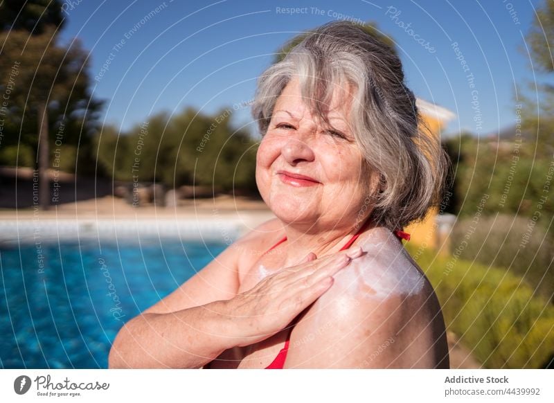 Smiling old woman smearing lotion while relaxing on poolside senior sunbath sunblock cream apply positive hydrate chill female carefree water gray hair summer