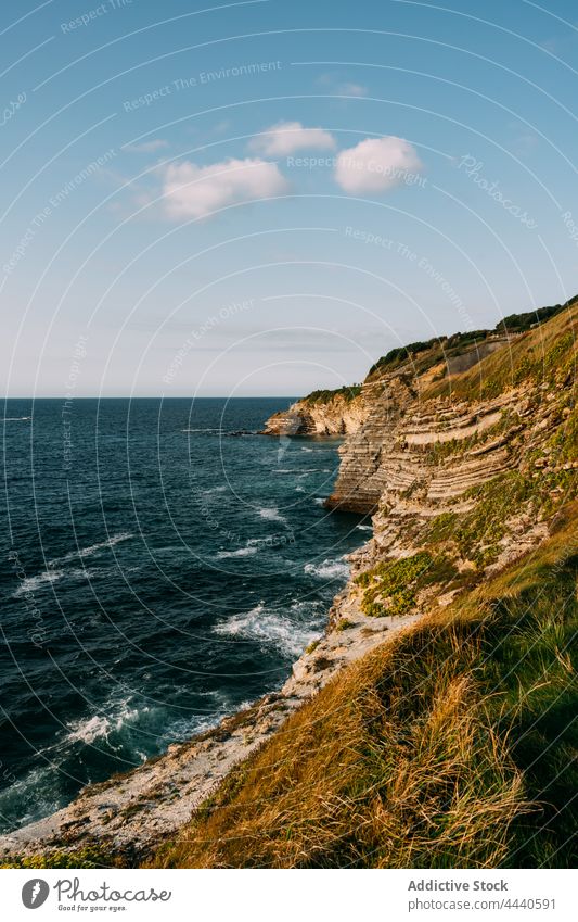 Cliff against wavy ocean under cloudy sky sea cliff blue sky nature seascape highland landscape horizon stormy weather foamy ripple seawater rock rough