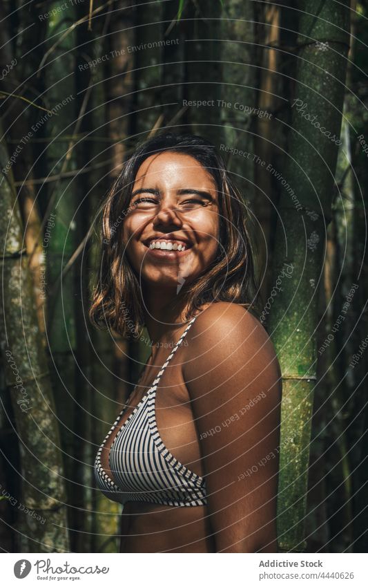 Smiling tourist in swimsuit against bamboo plants traveler smile swimwear vacation trip sincere natural shadow woman cheerful twig tourism candid stripe