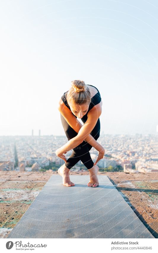 Woman practicing yoga on mat in city woman forward bend legs crossed wellness healthy lifestyle vitality energy practice rooftop prepare pose lean forward urban