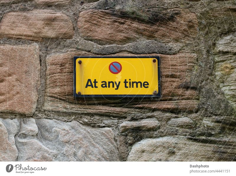 No Parking At Any Time Sign on an Old Stone Town Centre Wall sign signage road sign traffic sign roadside sign warning advice instruction notice yellow red