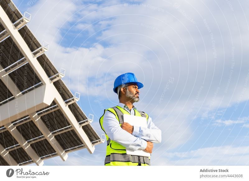 Hispanic engineer in helmet with clipboard working on solar power station man foreman building ecology energy plant farm photovoltaic technician alternative