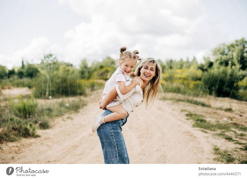 A young mother rolls her little daughter on her back, the baby hugs her mother ride happy girl mom woman lifestyle countryside female caucasian beautiful