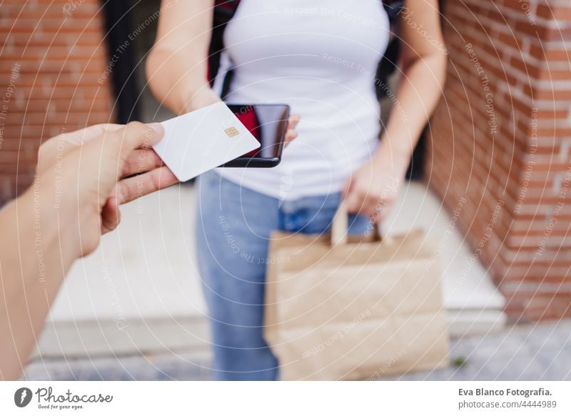 unrecognizable woman in street paying with credit card to rider woman delivering food in bicycle. Deliver food concept and sustainable transport city outdoors