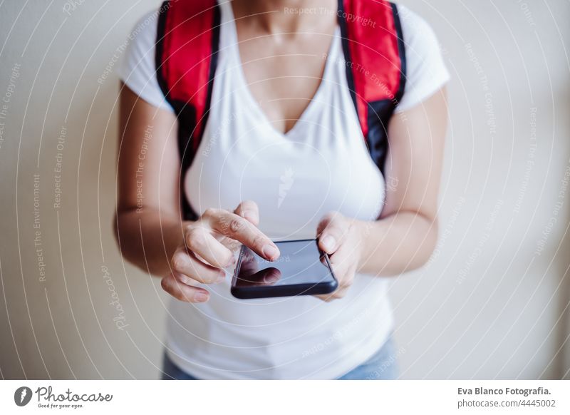 unrecognizable rider woman wearing red backpack delivering food, checking order with smart phone while standing on street in city. Delivery service concept. Sustainable transport