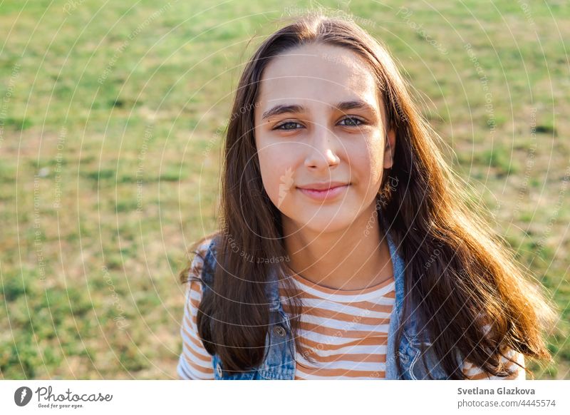 A beautiful and cheerful teenage student girl with long brown hair, in a striped long sleeve shirt and a denim vest walks in an autumn park. Natural lighting golden hour Generation Z