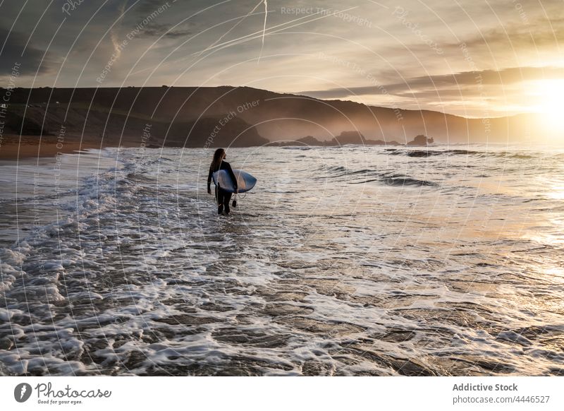 Woman with surfboard getting into the sea during sunset woman sunrise wetsuit sportswoman fun silhouette waves sunshine female vacation surfer water surfing