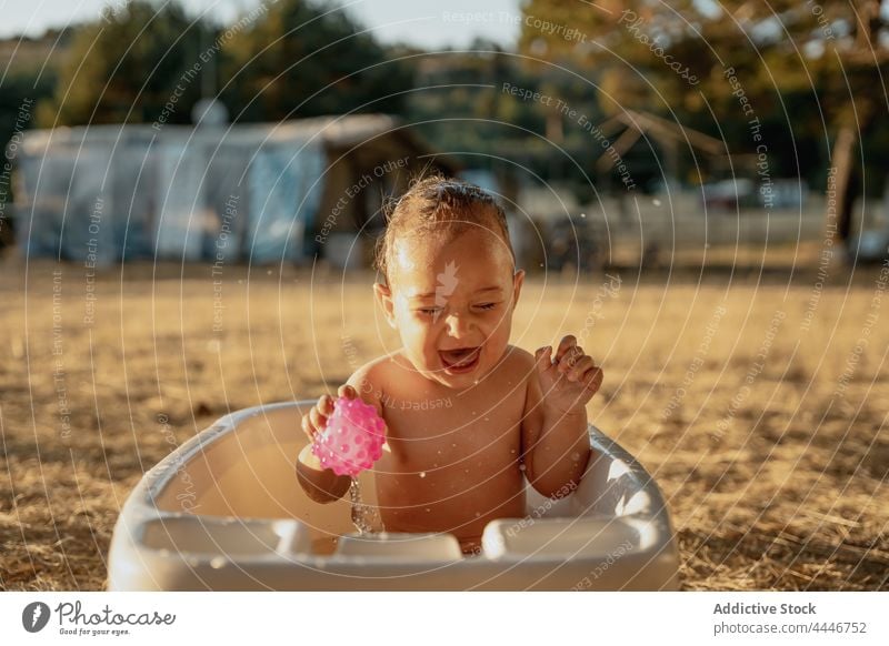 Cheerful baby having fun in small bath play cheerful carefree eyes closed toy drop countryside innocent child toddler glad drip babyhood enjoy laugh cute kid