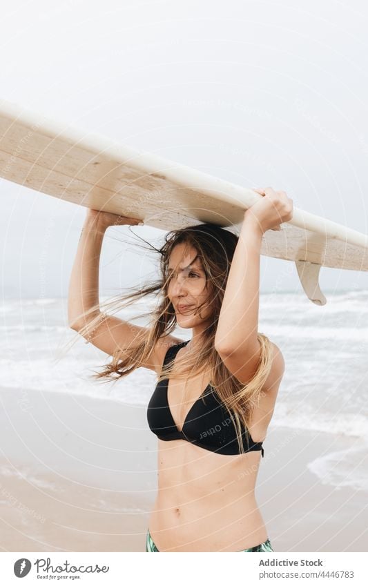 Surfer with surfboard on head on sea beach surfer flying hair sport body swimwear surfing enjoy woman seashore sky swimsuit smile coast stormy ocean contemplate