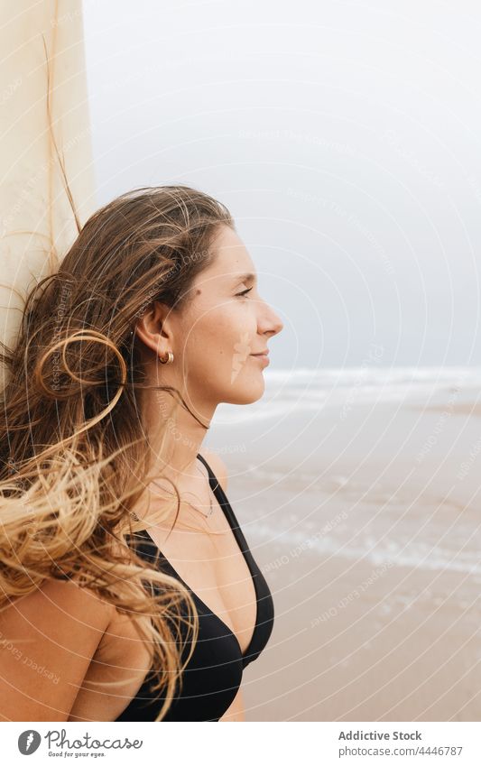 Pensive surfer with surfboard on sea shore thoughtful pensive sport surfing flying hair swimsuit woman seacoast sky body swimwear enjoy seashore smile stormy