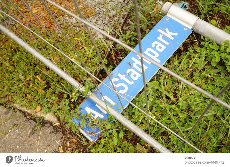 blue street name sign - Am Stadtpark - lies under a barrier on the lawn Street sign aborted Protective Grating Orientation Vandalism street sign conversion