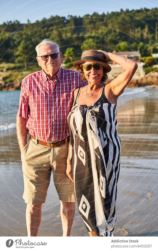 Senior couple standing on beach by waving sea senior positive sand love nature wife husband seacoast smile together relationship water bay embrace shore summer