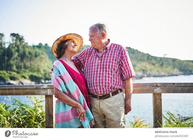 Elderly man standing with wife enjoying seascape couple senior together love positive shore nature husband relationship sunshine embrace elderly water sunlight