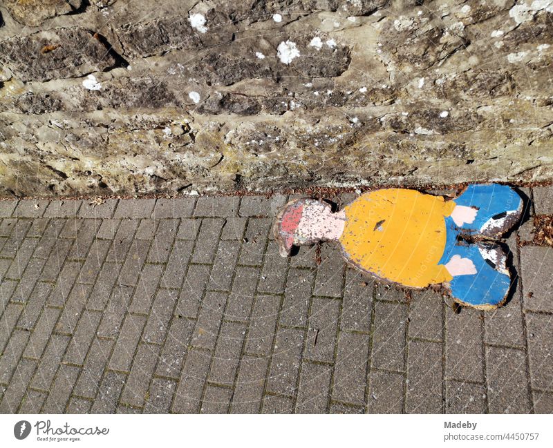 Stylized depiction of a sitting boy with a red cap, painted on a chipboard, on the paved sidewalk in the sunshine in Oerlinghausen near Bielefeld on the Hermannsweg in the Teutoburg Forest in East Westphalia-Lippe