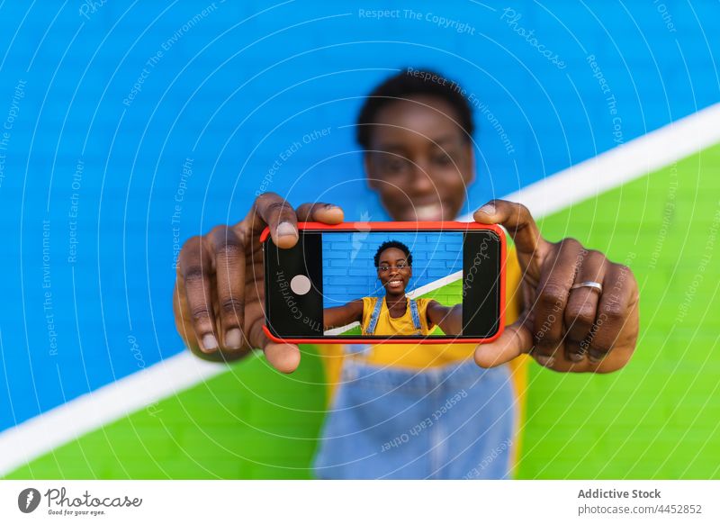 Smiling black woman taking selfie on smartphone using glad enjoy colorful capture photo screen female device happy self portrait delight digital cellphone