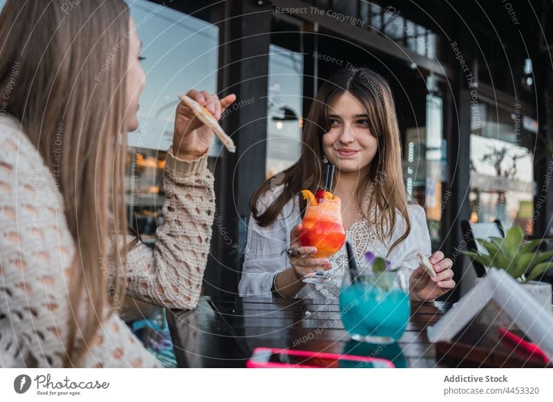 Crop smiling teens with cocktails talking in urban cafe best friend snack gather drink beverage content street girlfriend glass refreshment smile spend time