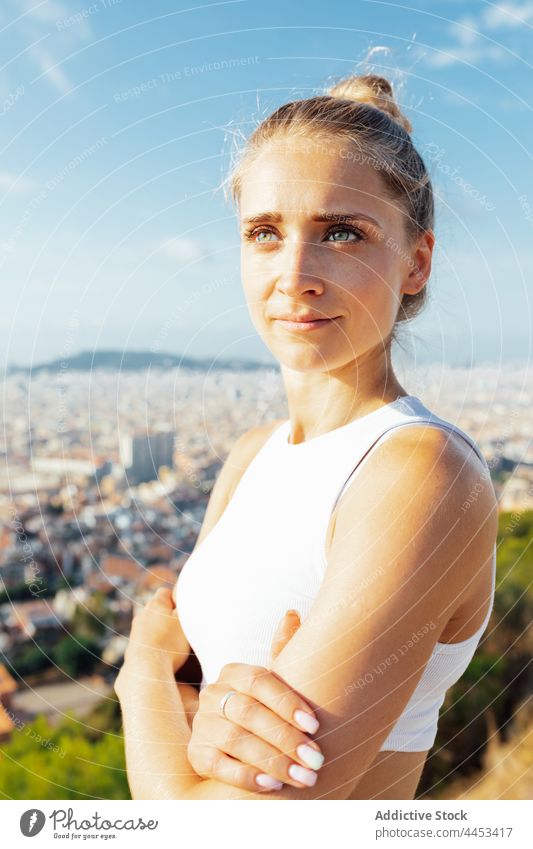 Sportswoman with crossed arms contemplating town in sunshine sportswoman arms crossed confident dreamy sporty healthy lifestyle wellness vitality blue sky