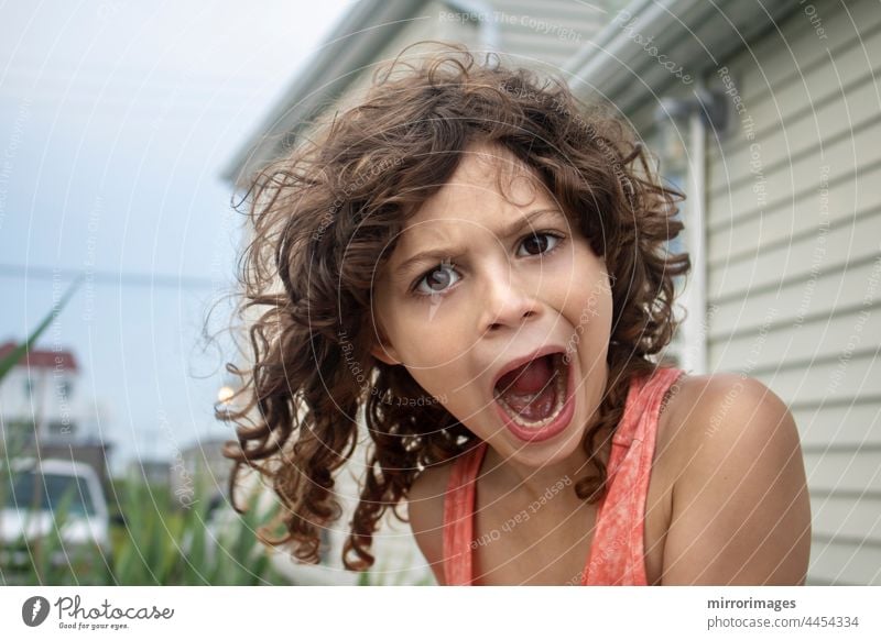 Little girl with currly brown hair making silly faces at camera with open mouth positive children summer close-up enjoyment daughter summertime sunshine