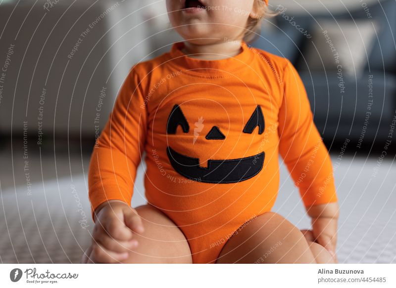 Happy baby one year old in orange Halloween costume at home halloween 2-3 months cry gas health newborn care colic skin child pumpkin massage trick or treat