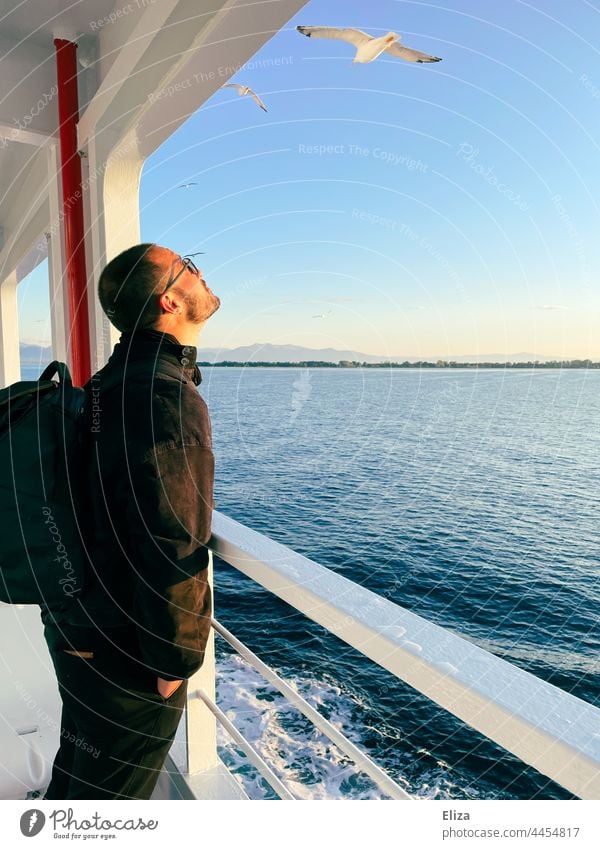 A man stands at the railing of a ferry and watches the passing seagulls Ferry Railing Man Observe Crossing Passenger ship Trip On board Ocean Freedom Navigation