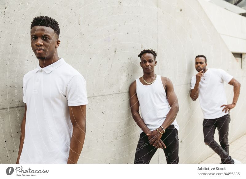 Black male friends in stylish outfits standing near concrete wall men cool style masculine trendy modern confident thoughtful individuality posture appearance