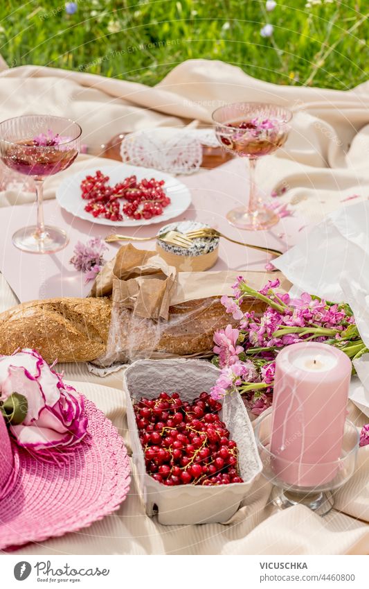 Aesthetic picnic with baguette, glasses of champagne, berries,  cheese , candles and pink flowers bunch on beige blanket. Outdoor aesthetic outdoor aesthetics