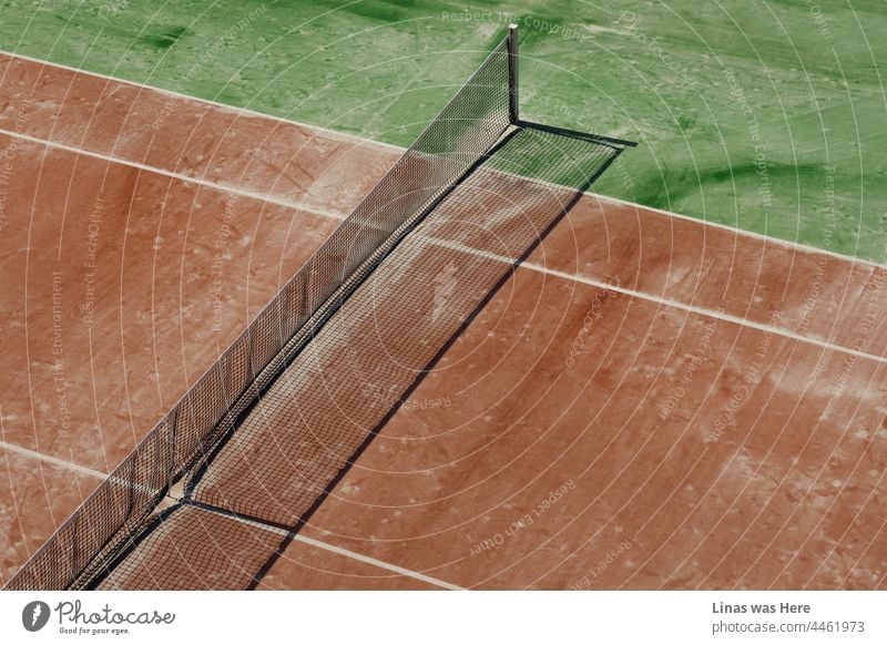 Time to take a break from tennis and leave the court alone. The abandoned and moody atmosphere in the image. No players around. Only a dirty playground, rusty net, and the shadows of the hot noon.