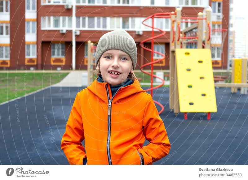 Funny caucasian blond boy in an orange jacket plays on the sports playground happy childhood outdoors teen kid smiling fun park playing school day schoolyard