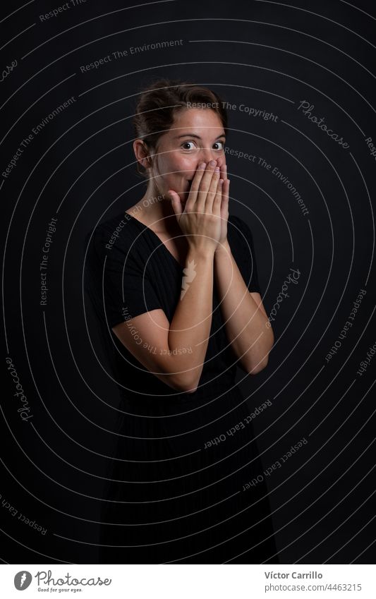 A young beautiful woman surprised by something in a studio shot in black dress and background 20-25 adult attractive beauty brunette casual close-up concepts