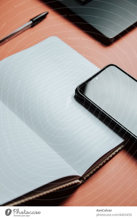 Blank notepad is on top of color office desk table with laptop computer, phone and supplies. Top view with copy space, flat lay. Minimal concept, work space