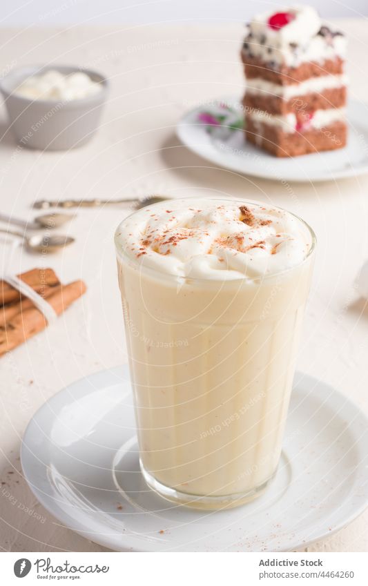 Eggnog cocktail against cake piece in cafe eggnog drink beverage cinnamon whipped egg white sweet glass cafeteria delicious dessert treat milk punch egg yolk