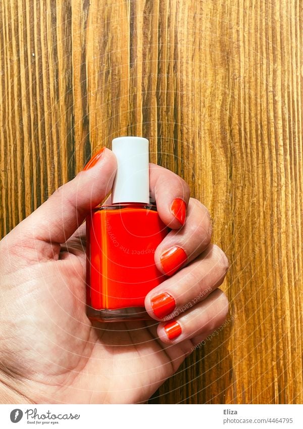 Woman with red painted fingernails holds a bottle with red nail polish Nail polish Red lacquered nails Feminine Manicure Hand Wood stop