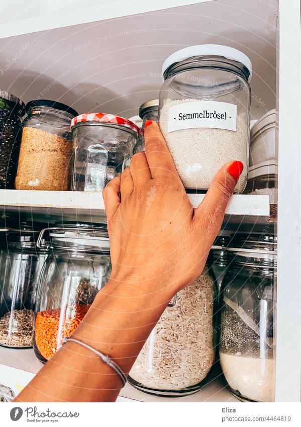 Hand reaches for a labeled storage jar of breadcrumbs in a kitchen cabinet Storage Vessels storage jars kitchen cupboard Food Inventories Kitchen