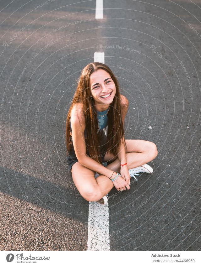 Cheerful teen with crossed legs on road teenage cheerful legs crossed friendly kind sincere charming rest portrait smile enjoy asphalt marking line roadway