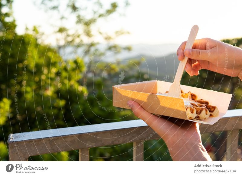 Anonymous person enjoying delicious waffles against mountains in sunshine eat dessert treat cream whipped sweet takeaway box spoon belgian tasty smooth aroma