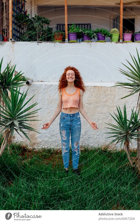 Happy woman standing on grass between palms meditate zen gesture happy carefree exotic enjoy lawn female cheerful optimist toothy smile tree delight plant