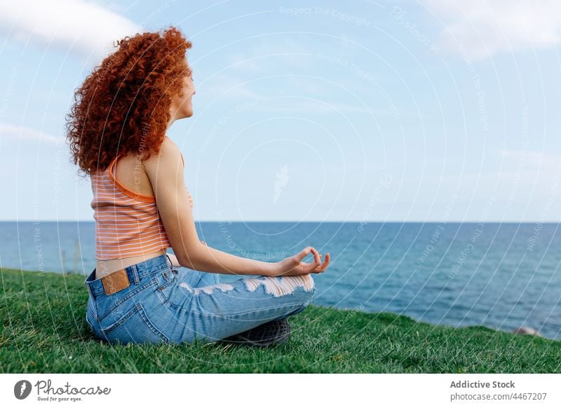 Young woman sitting in Lotus pose and meditating on grass meditate lotus pose sea asana hill zen harmony yoga stress relief female padmasana mental carefree