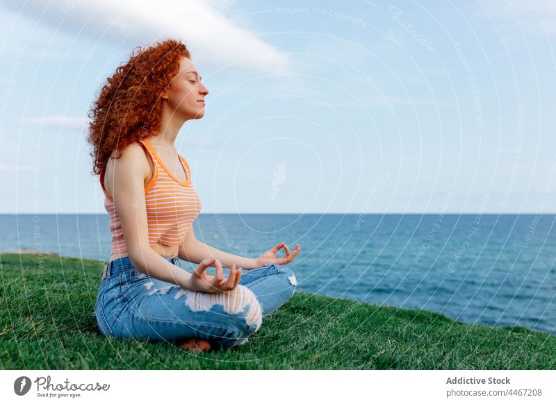 Young woman sitting in Lotus pose and meditating on grass meditate lotus pose sea asana hill zen harmony yoga stress relief female padmasana mental carefree