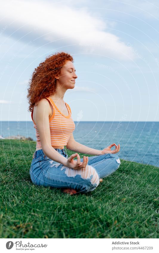 Young woman sitting in Lotus pose and meditating on grass meditate lotus pose sea asana hill zen harmony yoga stress relief female padmasana mental carefree