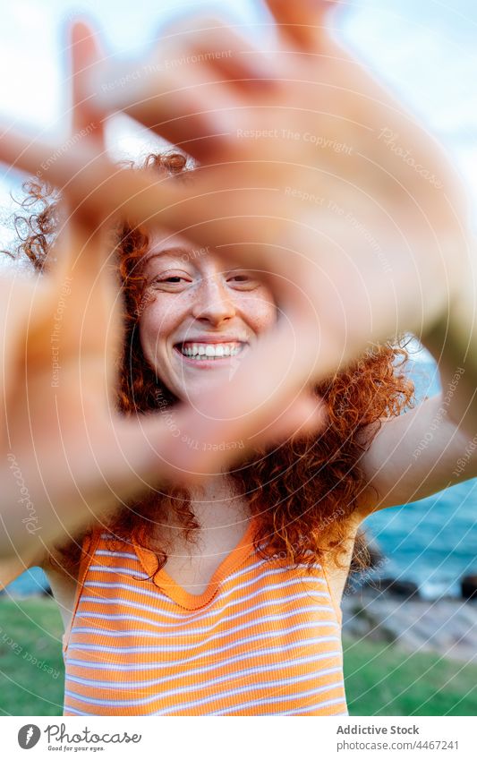 Smiling woman showing triangle gesture near sea coast shape positive happy holiday enjoy female seashore stone curly hair boulder long hair appearance nature