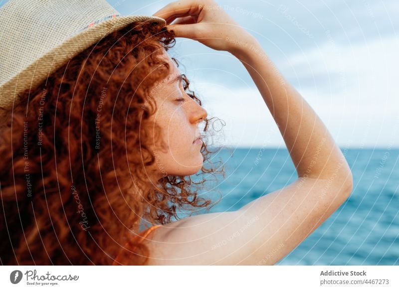 Woman with hat and eyes closed on seashore woman hide cover face coast freckles posture playful peaceful enjoy admire nature secret female curl redhead water