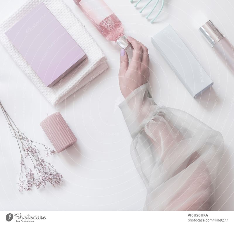 Women hand holding pink  cosmetic bottle on modern beauty  background with packaging boxes, candles and flowers. Top view. Pastel muted color women top view