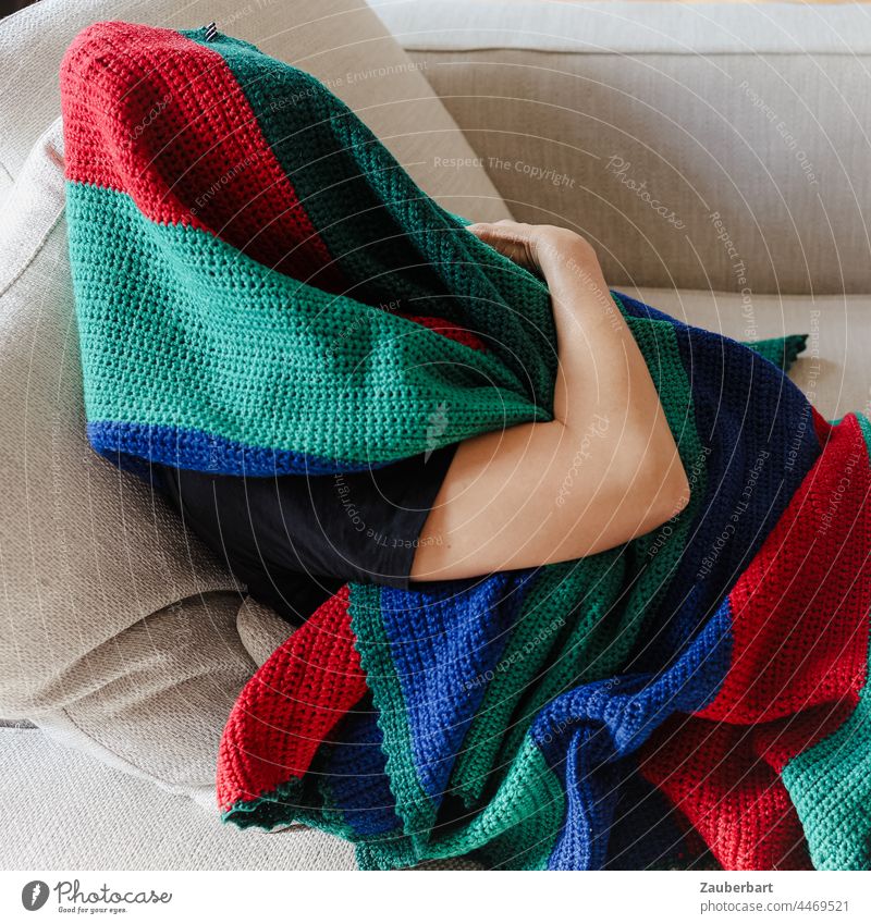 Man hiding under a colorful wool blanket on the sofa Human being arm Wool blanket variegated Sofa wrapped Green Red Blue stop Hide crease Textiles Cloth