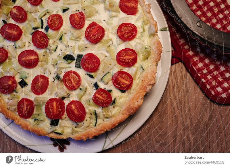 Vegetable quiche with cherry tomatoes, zucchini and leek on plate, checkered pot holder Quiche vegetable quiche Vegetable Cake Cherry Tomatoes Oven cloth Red