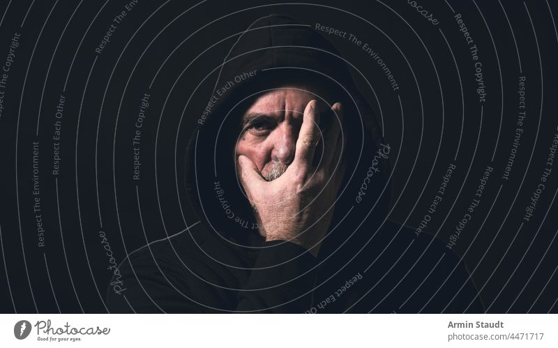 portrait of a man with a hoodie holding a hand in front of his face angle beard black blur breath casual caucasian close-up closeup confident cool corona cover