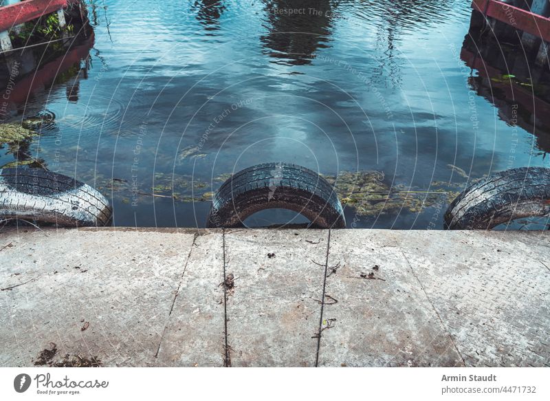 three old car tires as ram protection in a small harbor abandoned background concrete construction detail dirt grunge lake landing landscape nature outdoor